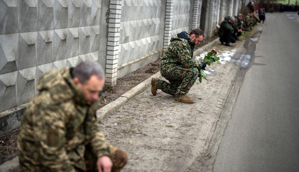 Tentara Ukraina berlutut menunggu peti mati Oleksandr Maksymenko (38) lewat saat pemakamannya di kampung halamannya di Kniazhychi, sebelah timur Kyiv, Ukraina, 13 Februari 2023. Oleksandr Maksymenko, seorang warga sipil yang menjadi sukarelawan di angkatan bersenjata Ukraina, tewas dalam pertempuran di daerah Bakhmut. (AP Photo/Emilio Morenatti)