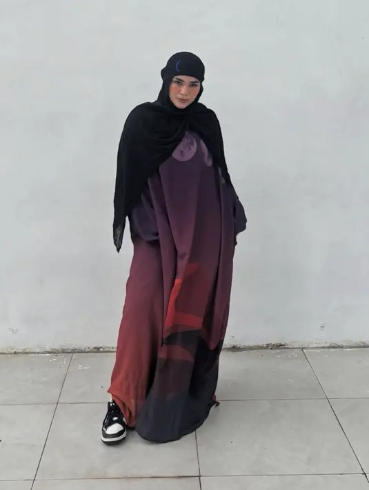 Selanjutnya, Sivia mengenakan pashmina hitam panjang polos dipadukan abaya warna gradasi merah hitam dengan corak serta mengenakan sneakers Nike hitam putih.  [@siviazizah]