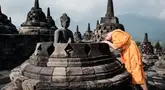Seorang biksu Buddha berdoa di depan patung di salah satu stupa Candi Borobudur di Magelang, Jawa Tengah, pada 10 Mei 2025. (YASUYOSHI CHIBA/AFP)