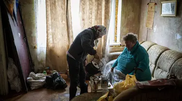 Lyubov Lomachuk (69) menyajikan teh untuk tetangganya Valentyna Volynets (59) setelah merebus air di api darurat di taman umum dekat gedung mereka di Bucha, Kiev, Senin (18/4/2022). Warga Bucha masih tanpa listrik, air dan gas setelah lebih dari 43 hari sejak invasi Rusia (AP Photo/Emilio Morenatti)
