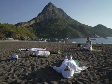 Orang-orang berlatih yoga di pantai di Adrasan, barat Antalya, Turki (24/9/2021). Orang-orang menikmati cuaca hangat di wilayah Mediterania saat salju pertama menyelimuti pegunungan tinggi di timur laut Turki. (AP Photo/Burhan Ozbilici)