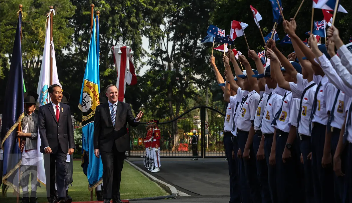 Presiden Joko Widodo berjalan bersama Perdana Menteri Selandia Baru John Key disambut pelajar yang mengibarkan bendera saat upacara penyambutan di Halaman Istana Merdeka, Jakarta, Senin (18/7). (Liputan6.com/Faizal Fanani)