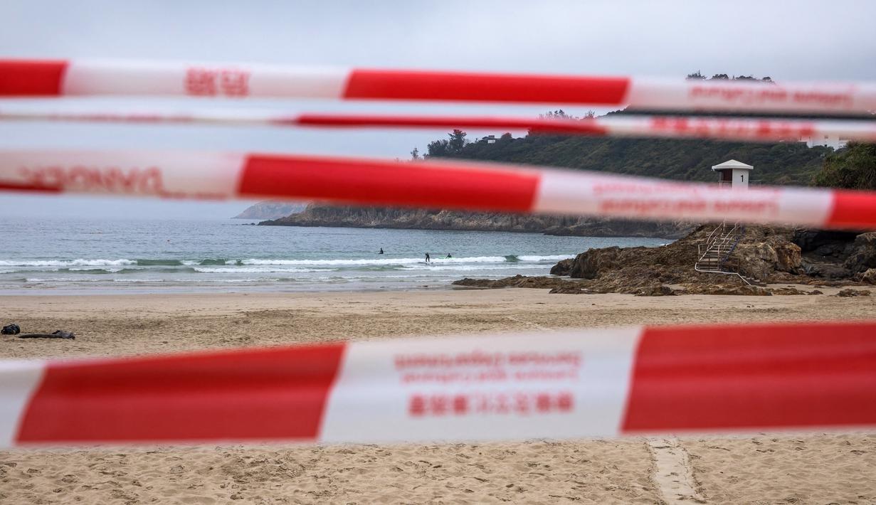Orang-orang berselancar ketika para pekerja mulai menutup Pantai Big Wave Bay di Hong Kong, Kamis (17/3/2022). Pemerintah Hong Kong mengatakan akan menutup pantai umum untuk mengekang penyebaran virus corona COVID-19. (DALE DE LA REY/AFP)
