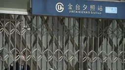Seorang pekerja yang mengenakan masker berdiri di dalam gerbang pintu keluar stasiun kereta bawah tanah yang tertutup di Beijing, China Rabu (4/5/2022). Beijing pada hari Rabu ini menutup lebih dari 40 stasiun kereta bawah tanah, sekitar sepersepuluh dari jaringan kereta, sebagai bagian dari tindakan untuk menghentikan penyebaran Covid-19. (AP Photo/Mark Schiefelbein)