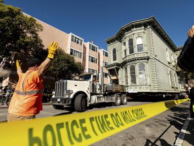 Pekerja memberi arahan kepada sopir truk yang sedang menarik rumah bergaya Victoria berusia 139 tahun di San Francisco, Minggu (21/2/2021). Rumah dua lantai yang dibangun pada tahun 1882 tersebut dipindahkan ke lokasi baru yang berjarak hanya enam blok.  (AP Photo/Noah Berger)