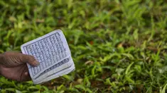 Seorang perempuan membaca Alquran pada peringatan 16 tahun gempa bumi dan tsunami Aceh di sebuah kuburan massal di Siron, Sabtu (26/12/2020).  Peringatan di tengah pandemi COVID-19 itu tetap berlangsung secara sederhana melalui kegiatan ziarah kubur. (CHAIDEER MAHYUDDIN/AFP)