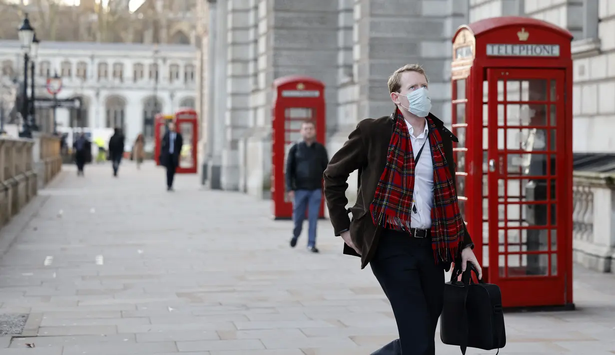 Seorang pria mengenakan masker untuk mengurangi penyebaran Covid-19, berjalan di sepanjang Whitehall di pusat kota London (5/1/2022). Rumah sakit Inggris telah kekurangan staf yang disebabkan oleh gelombang infeksi Omicron, kata pemerintah pada hari Selasa (4/1). (AFP/Tolga Akmen)