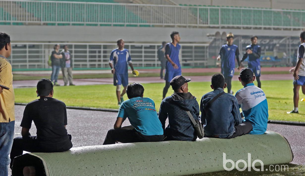 Pekerja beristirahat sejenak sambil menonton aksi para pemain Arema FC yang sedang berlatih di Stadion Pakansari, Bogor, Jumat (10/3/2017). Arema FC akan melawan Pusamania Borneo FC pada laga Final Piala Presiden 2017. (Bola.com/Nicklas Hanoatubun)