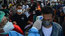 Petugas memeriksa suhu tubuh warga yang mengikuti vaksinasi virus corona COVID-19 AstraZeneca di Denpasar, Bali, Sabtu (26/6/2021). Ratusan warga terlihat antusias mengikuti vaksinasi massal tersebut. (SONY TUMBELAKA/AFP)