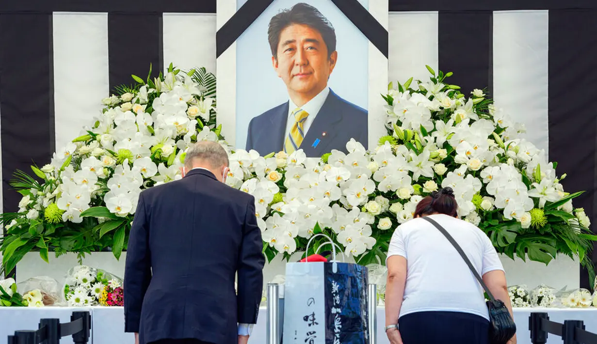 Orang-orang meninggalkan bunga dan memberi penghormatan kepada mantan Perdana Menteri Jepang Shinzo Abe jelang pemakaman kenegaraannya di luar Nippon Budokan, Tokyo, Jepang, 27 September 2022. Di luar arena pemakaman Abe, ribuan orang mengantre pada Selasa pagi ini untuk meletakkan bunga dan memberi penghormatan. (Nicolas Datiche/Pool Photo via AP)
