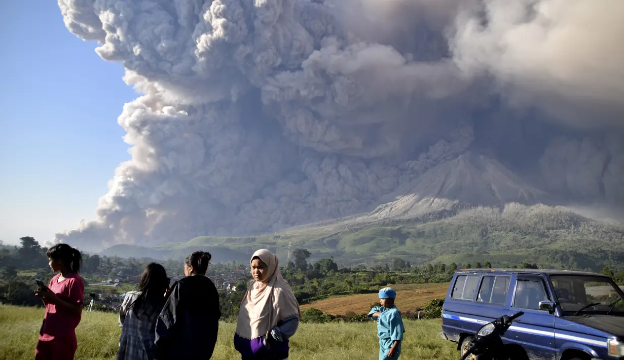 Orang-orang menyaksikan Gunung Sinabung memuntahkan material vulkanik saat meletus di Karo, Sumatera Utara, Selasa (2/3/2021).  Gunung Sinabung, Sumatera Utara, memuntahkan awan panas pada pukul 07.11 WIB, Selasa (2/1/2021). (AP Photo)