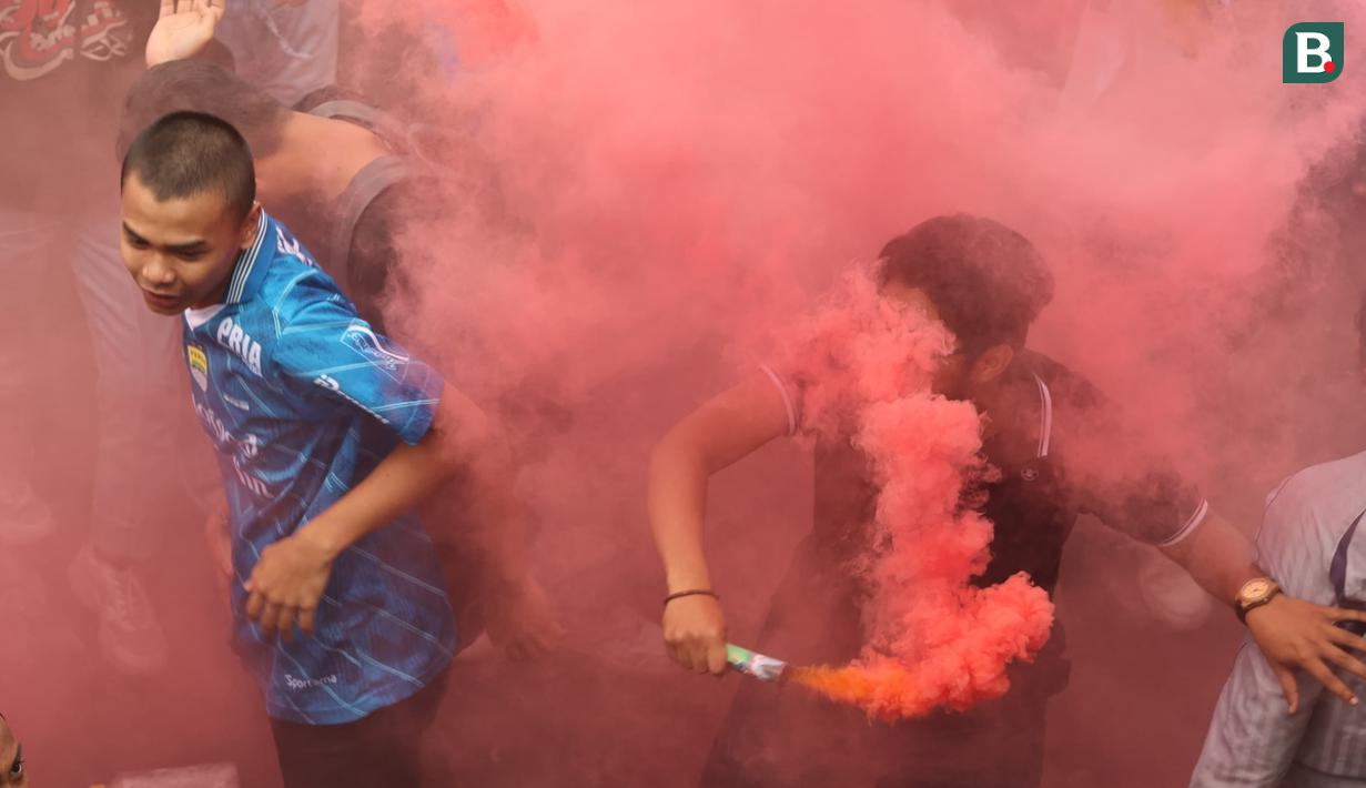 Seorang fans menyalakan suar saat melakukan pawai di Kota Bandung, Sabtu (1/6/2024) untuk menyambut kedatangan skuad Persib Bandung usai menjadi juara Championship Series BRI Liga 1 2023/2024. (Bola.com/M Iqbal Ichsan)