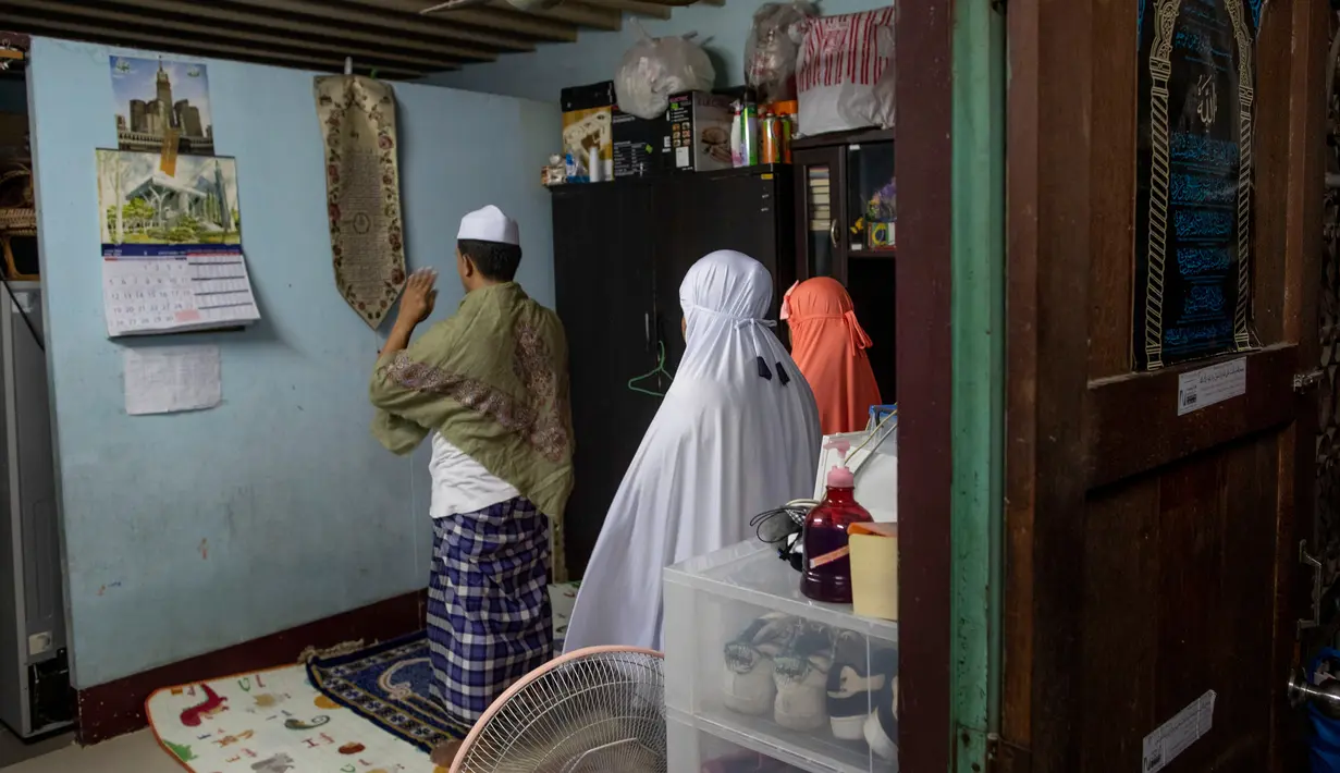 Keluarga Muslim Thailand melaksanakan salat setelah berbuka puasa di ruang tamu rumah mereka di Bangkok, pada 28 April 2020. Banyak tempat ibadah ditutup guna membendung penyebaran Virus Corona COVID-19 ketika Umat Muslim di seluruh dunia menyambut bulan suci Ramadan. (AP Photo/Gemunu Amarasinghe)