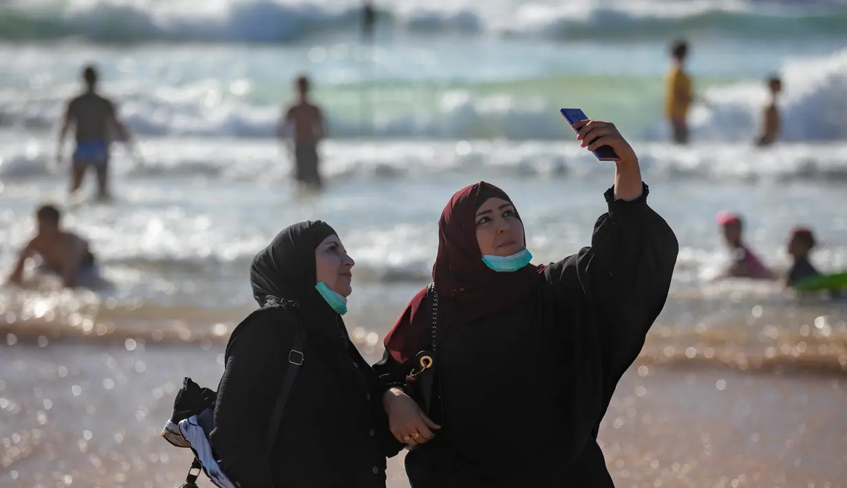 Wanita Palestina berselfie selama liburan Idul Fitri, di pantai laut Mediterania di Tel Aviv, Israel (25/5/2020).  Idul Fitri menandai akhir bulan suci Ramadhan, perayaan tiga hari yang biasanya menggembirakan telah berkurang secara signifikan karena pandemi coronavirus. (AP Photo/Oded Balilty)