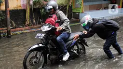 Pengendara motor terpaksa mendorong kendaraannya yang mengalami mati mesin saat mencoba melewati genangan air di jalan Bangun Nusa Raya, Cengkareng, Jakarta Barat. (Magang/Liputan6.com/Muhammad Rizal)