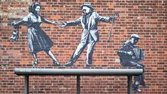 Sebuah karya seni grafiti dari pasangan yang menari dengan pemain akordeon, yang menyandang ciri khas seniman jalanan Banksy, terlihat di dinding di Great Yarmouth di pantai timur Inggris pada 8 Agustus 2021. Karya tersebut belum diklaim oleh Banksy. (JUSTIN TALLIS / AFP)