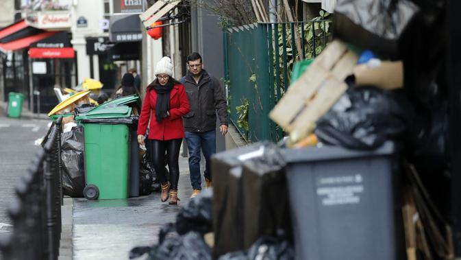 Orang-orang berjalan melewati tong sampah dan tumpukan kantong sampah yang menumpuk di Paris (4/2/2020). Serikat pekerja memutuskan kegiatan di pabrik pembakaran kunci untuk memprotes reformasi yang mereka katakan tidak adil. (AP Photo/Christophe Ena)