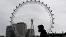 Seorang pria memakai masker saat melewati London Eye di London, Kamis (29/10/2020). Sekitar 100.000 orang terjangkit virus corona setiap hari di Inggris, menurut studi terbaru Imperial College London. (AP Photo/Frank Augstein)