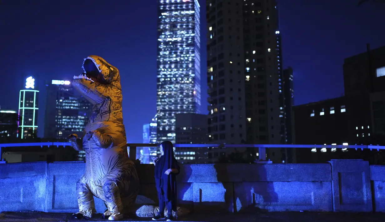 Seorang pria berpakaian dinosaurus berdiri di daerah Mid-Level di Hong Kong, Kamis (31/10/2019). Para pemrotes Hong Kong menyerukan kepada orang-orang untuk menandai Halloween dengan mengenakan topeng yang menggambarkan pejabat pemerintah atau tokoh-tokoh menakutkan. (AP Photo/Vincent Yu)
