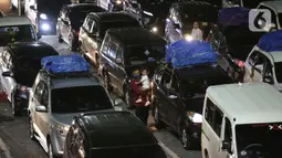 Seorang pria sambil menggendong anak melintas di antara mobil pribadi yang akan menyeberang ke Pulau Sumatera terjebak kemacetan sebelum masuk ke kapal "Roll on-Roll off" (RoRo) di Pelabuhan Merak, Banten, Kamis (28/4/2022). Jelang hari raya Idul Fitri, pemudik dengan kendaraan bermotor mulai memadati Pelabuhan Merak. Penumpukan kendaraan ini menyebabkan terjadinya antrean kendaraan yang panjang. (Liputan6.com/Angga Yuniar)