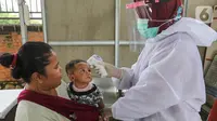 Bidan lengkap dengan baju Alat Pelindung Diri (APD) mengukur suhu tubuh pada anak di Posko Imunisasi, Kelurahan Bakti Jaya, Tangerang Selatan, Senin (11/5/2020). Pelayanan imunisasi tetap berjalan sesuai jadwal meski pandemi Covid-19. (Liputan6.com/Fery Pradolo)
