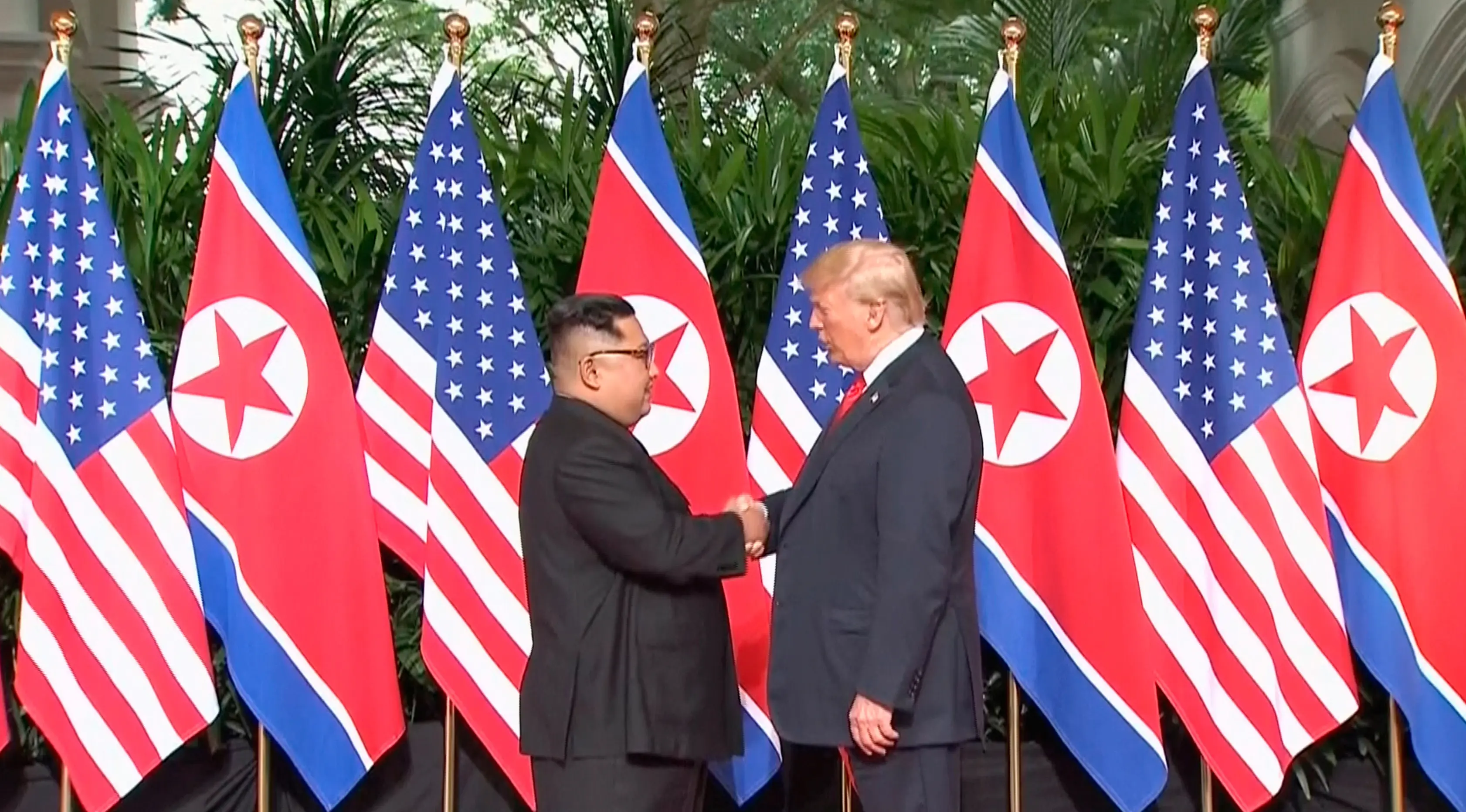 Presiden AS Donald Trump  berjabat tangan dengan Pemimpin Korea Utara, Kim Jong-un dalam pertemuan bersejarah di resor Capella, Pulau Sentosa, Selasa (12/6). Trump dan Kim berjabat tangan untuk pertama kalinya. (Host Broadcaster Mediacorp Pte Ltd via AP)