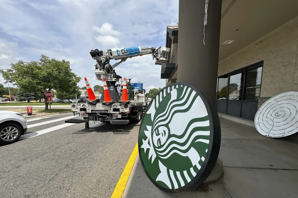 Seorang pekerja membongkar papan nama Starbucks