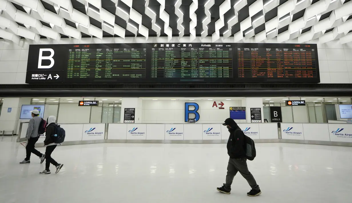 Penumpang berjalan di depan layar jadwal kedatangan penerbangan internasional di Bandara Narita, Tokyo, Kamis (2/12/2021). Maskapai-maskapai internasional diminta menangguhkan reservasi baru pada semua penerbangan masuk ke Jepang hingga akhir Desember terkait varian Omicron. (AP Photo/Hiro Komae)