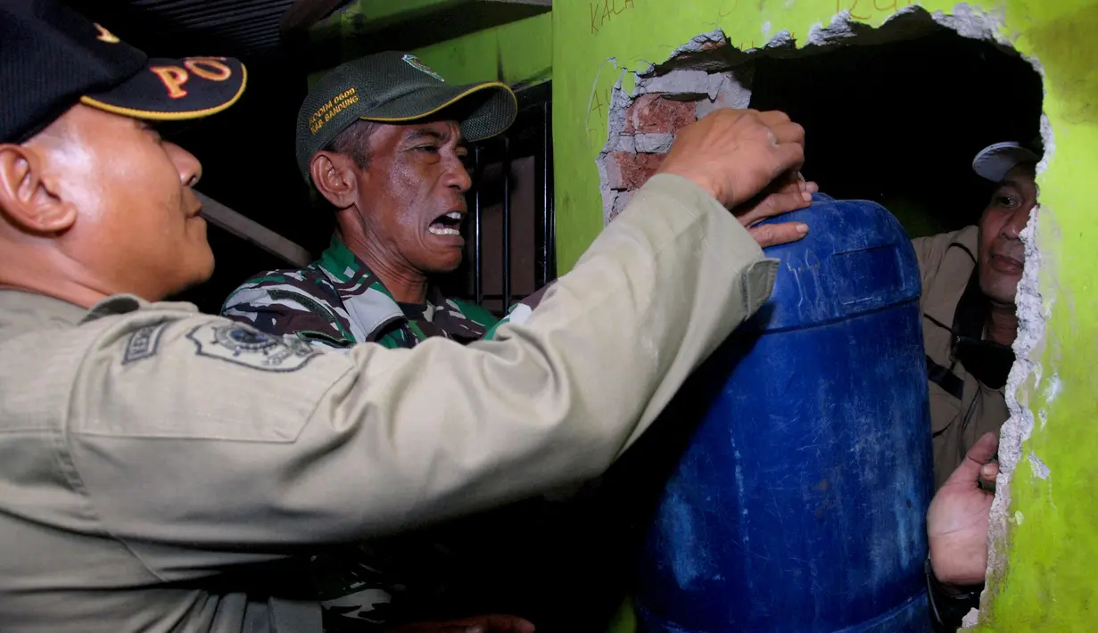 Petugas membawa jerigen yang berisi bahan untuk miras oplosan saat melakukan penggerebekan di Cicalengka, Bandung, Minggu (8/4).  Sebanyak 15 dari 27 nyawa melayang usai meneguk minuman keras (miras) oplosan di Cicalengka. (Timur Matahari/AFP)