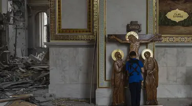 Seorang anak laki-laki mencium patung Yesus saat membantu membersihkan Katedral Transfigurasi Odesa setelah gereja rusak berat akibat serangan rudal Rusia di Odesa, Ukraina, Minggu, 23 Juli 2023. (AP Photo/Jae C. Hong)