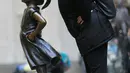 Seorang wanita berpose dengan patung "Fearless Girl" di lokasi barunya di depan bursa efek New York, Selasa (11/12). Kini patung perunggu yang sempat menimbulkan kontroversi itu mendapatkan rumah baru yang lebih permanen. (AP/Mark Lennihan)