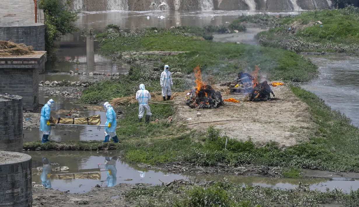 Petugas mengenakan pakaian pelindung membawa jenazah korban COVID-19 untuk dikremasi di tepi Sungai Bagmati dekat kuil Pashupatinath, Kathmandu, Nepal (3/5/2021). Lonjakan infeksi di Nepal telah mendorong pemerintah memberlakukan lockdown baru di kota besar dan kecil. (AP Photo/Niranjan Shrestha)