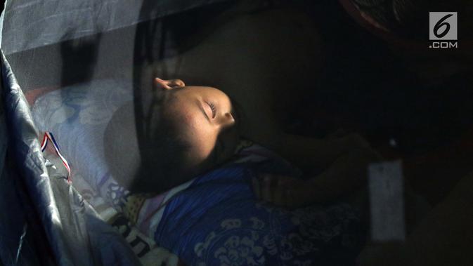 Seorang anak pencari suaka tertidur di dalam tenda di atas trotoar depan Masjid Ar-Rayan, Jalan Kebon Sirih, Jakarta, Jumat (5/7/2019). Para pencari suaka ini membangun tenda-tenda dan meminta kepastian perlindungan dari UNHCR . (Liputan6.com/Helmi Fithriansyah)