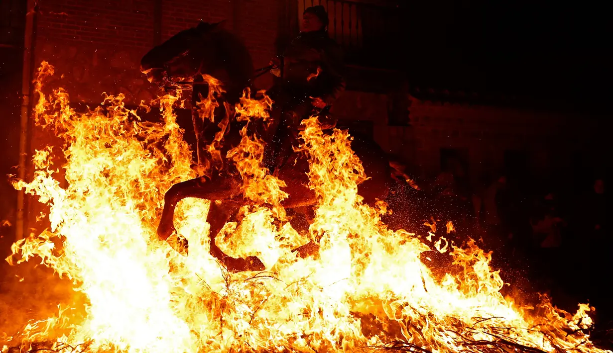 Seorang pria menunggangi kuda melewati api unggun saat festival Luminarias di San Bartolome de Pinares, Spanyol, Jumat (16/1/2020). Festival tersebut digelar setiap tahunnya, sehari sebelum perayaan Santo Antonius yang merupakan pelindung binatang. (AP Photo/Manu Fernandez)
