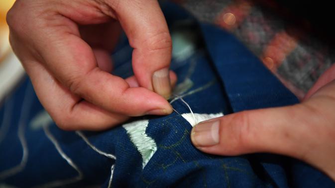 Seorang perempuan dari kelompok etnis Li memperagakan keahlian membuat bordir dengan pola naga dalam pameran selimut quilt di Museum Hainan, China pada 13 November 2020. Pameran yang berlangsung sebulan penuh tersebut menampilkan 41 selimut quilt dengan bordir naga Li yang indah. (Xinhua/Guo Cheng)
