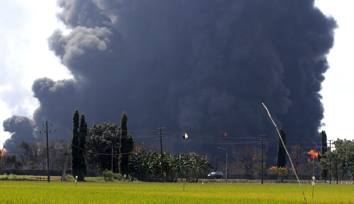 Sebuah mobil melintas sebagai kepulan asap dari kebakaran yang melanda Kilang Pertamina Balongan di Indramayu, Jawa Barat, Senin (29/3/2021). Ratusan orang dievakuasi dari desa terdekat setelah kebakaran besar terjadi di kilang tersebut. (AP Photo)