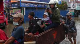 Pengendara bersama sepeda motornya berada di atas gerobak yang didorong pengojek gerobak saat melintasi banjir yang merendam jalan KH Hasyim Ashari, Kota Tangerang, Banten, Sabtu (16/7/2022). Warga sekitar membantu para pengendara yang melintas agar tidak terkena banjir dengan menawarkan jasa gerobak. (Liputan6.com/Angga Yuniar)