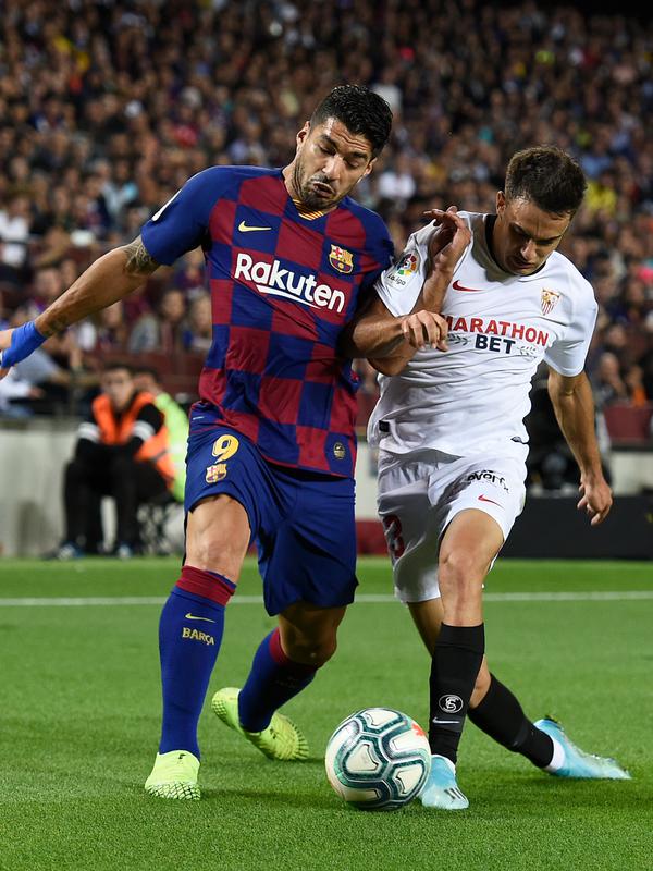 Penyerang Barcelona, Luis Suarez berebut bola dengan bek Sevilla Sergio Reguilon dalam pertandingan pekan kedelapan kompetisi La Liga Spanyol 2019-2020 di Camp Nou, Minggu (6/10/2019). Barcelona berhasil menang telak atas Sevilla dengan skor 4-0. (Josep LAGO / AFP)