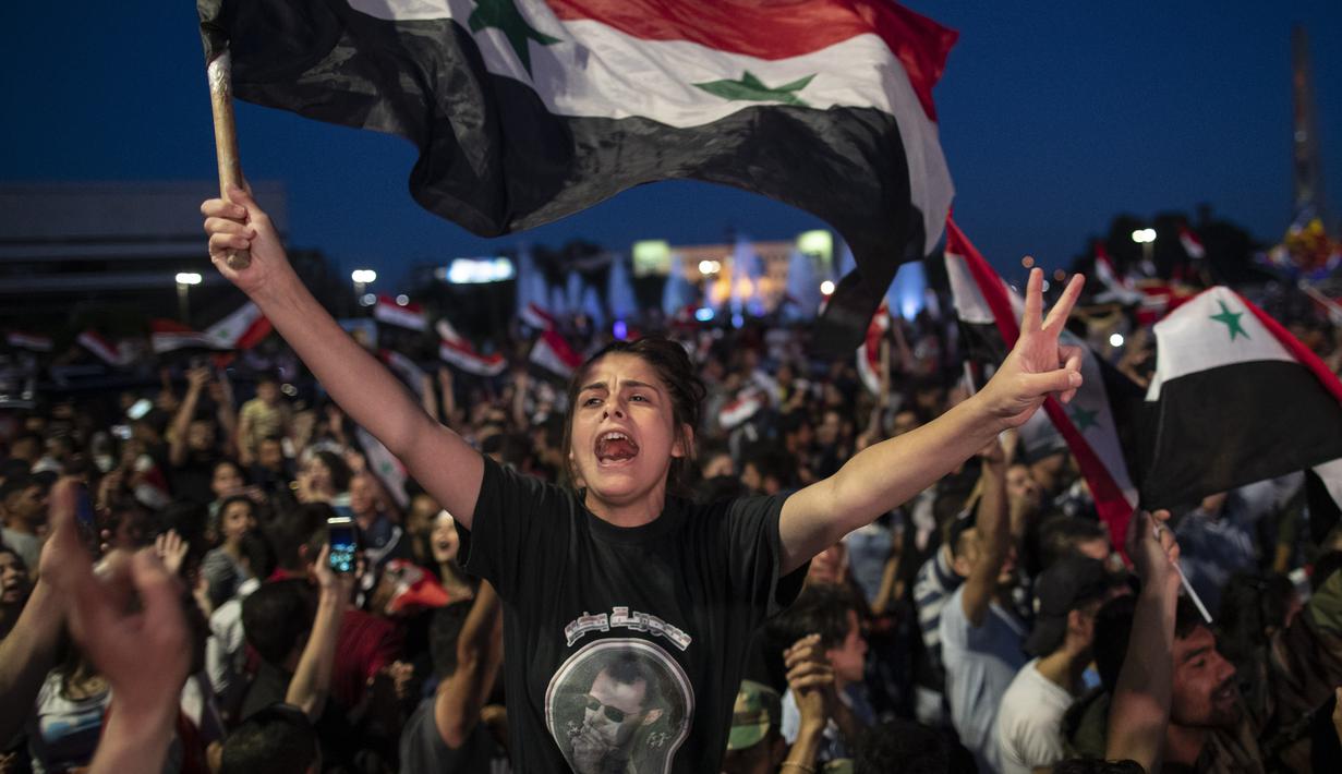 Pendukung mengibarkan bendera nasional dan foto Presiden Suriah Bashar Assad saat mereka merayakan kemenangannya di Omayyad Square, di Damaskus, Kamis (27/5/2021). Bashar al-Assad terpilih kembali untuk masa jabatan keempat sebagai presiden Suriah yang dilanda perang. (AP Photo/Hassan Ammar)