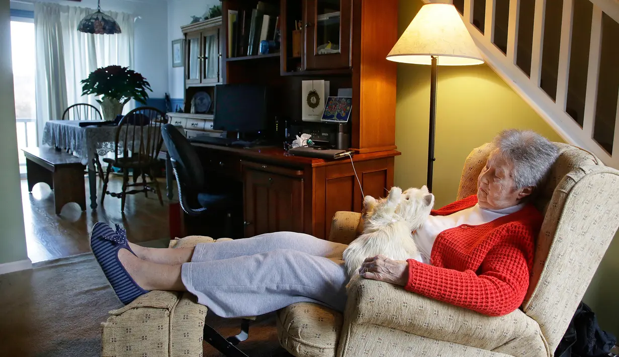 Mary Derr (93) duduk dengan robot kucing yang dipanggil "Buddy" di rumahnya, South Kingstown, 1 Desember 2017. Robot ini bisa berinteraksi serta memberikan respon dan cukup peka jika sang pemilik ingin bergurau dengannya. (AP/Stephan Savoia)
