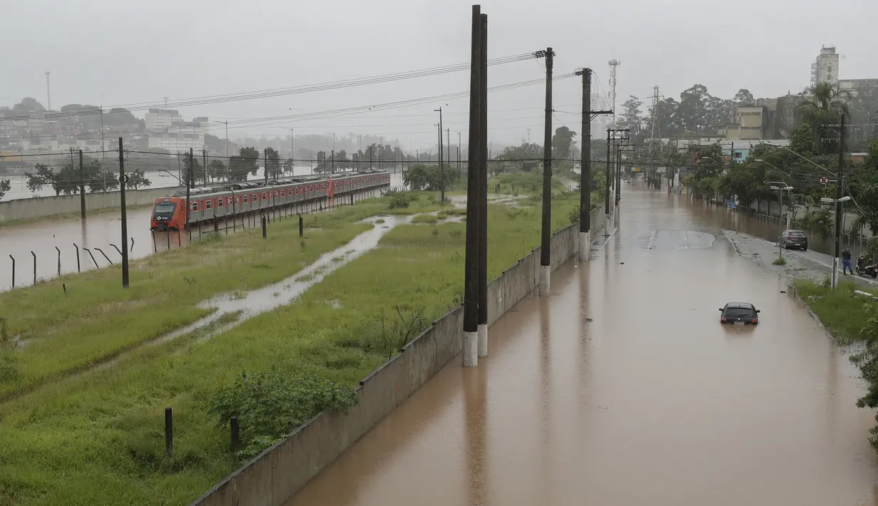 Sebuah kereta metropolitan terlihat di jalur rel yang banjir yang membentang di sepanjang sungai Pinheiros di Sao Paulo, Brasil, Senin, (10/2/2020). Hujan deras yang membanjiri kota, menyebabkan pinggir sungai utama meluap. (AP Photo/Andre Penner)