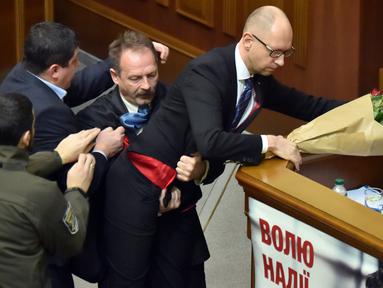 Seorang anggota parlemen bernama Oleg Barna tampak menyeret PM Arseny Yatsenyuk (kanan) dari podium saat membacakan laporan tahunan kinerja Pemerintah Ukraina di Majelis Tinggi Parlemen Ukraina, 11 Desember 2015. (Sergei SUPINSKY/AFP)