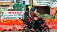 Warga melintasi pintu masuk kawasan Pasar Cileungsi yang dipenuhi spanduk penutupan, Kabupaten Bogor, Selasa (2/6/2020). Penutupan sementara kegiatan jual beli di Pasar Cileungsi terkait adanya tujuh pedagang yang positif terinfeksi virus COVID-19. (Liputan6.com/Helmi Fithriansyah)