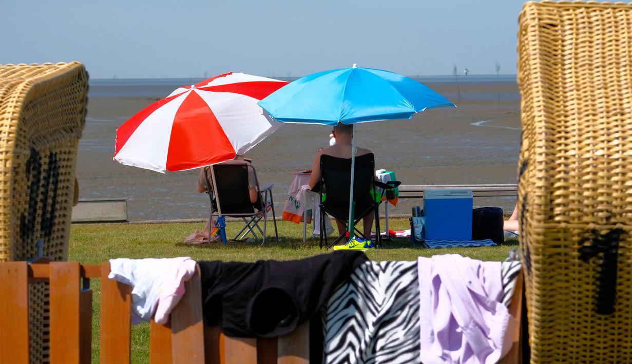 Warga duduk di bawah payung saat suhu mencapai 34 derajat Celcius di dekat pantai Laut Utara di Wremen, Jerman barat (24/7/2019). Peramal cuaca memprediksi suhu tertinggi di seluruh Eropa barat yang terkena gelombang panas akan mencetak rekor suhu terbaru.  (AFP Photo/Patrik Stollarz)