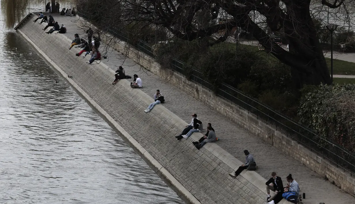 Orang-orang duduk di tepi sungai Seine di Paris, Rabu (3/3/2021).  Tingkat infeksi COVID-19 tetap tinggi selama beberapa minggu, dan pasien virus menempati 70% unit perawatan intensif negara itu. (AP Photo/Lewis Joly)