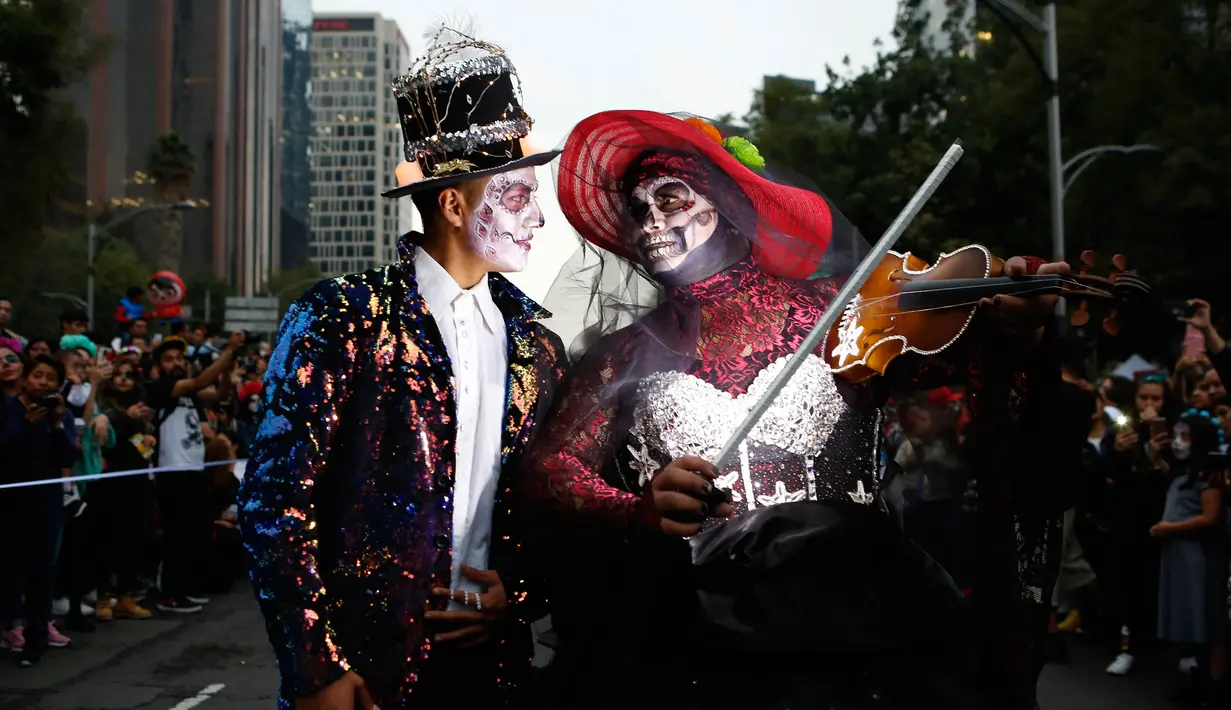 Sepasang peserta berdandan ala tengkorak saat mengikuti parade Hari Orang Mati di Mexico City, Meksiko, Sabtu (26/10/2019. Para peserta dalam parade ini mengenakan kostum dan melukis wajah mirip dengan tokoh tengkorak Meksiko yang ikonik, Catrina. (AP Photo/Ginnette Riquelme)