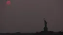 <p>Matahari terbenam di atas Patung Liberty di New York City, Amerika Serikat pada 22 Mei 2023. (Spencer Platt/Getty Images/AFP)</p>