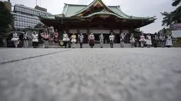Para karyawan yang mengenakan kostum pelayan dari beberapa kafe bertema pembantu di Akihabara berbaris di kantor polisi sebelum pertemuan doa untuk perlindungan dari COVID-19 dan untuk bisnis yang berkembang di kuil Kanda Myojin, Tokyo (25/7/2020). (AP Photo/Eugene Hoshiko)