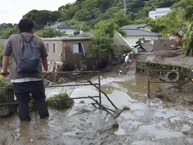 Seorang pria menyaksikan tim penyelamat melanjutkan operasi pencarian di lokasi tanah longsor di Izusan di Atami, prefektur Shizuoka, barat daya Tokyo,  Senin (5/7/2021). Evakuasi korban hilang terus dilakukan menyusul bencana tanah longsor akibat hujan lebat di kota tersebut. (Kyodo News via AP)