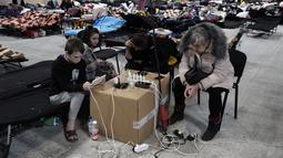 Warga Ukraina mengisi daya perangkat elektronik mereka di tempat penampungan pengungsi di Nadarzyn, dekat Warsawa, Polandia, Kamis (17/3/2022). Polandia telah menerima sekitar 1,95 juta pengungsi yang melarikan diri dari perang dan agresi Rusia di Ukraina. (AP Photo/Czarek Sokolowski)